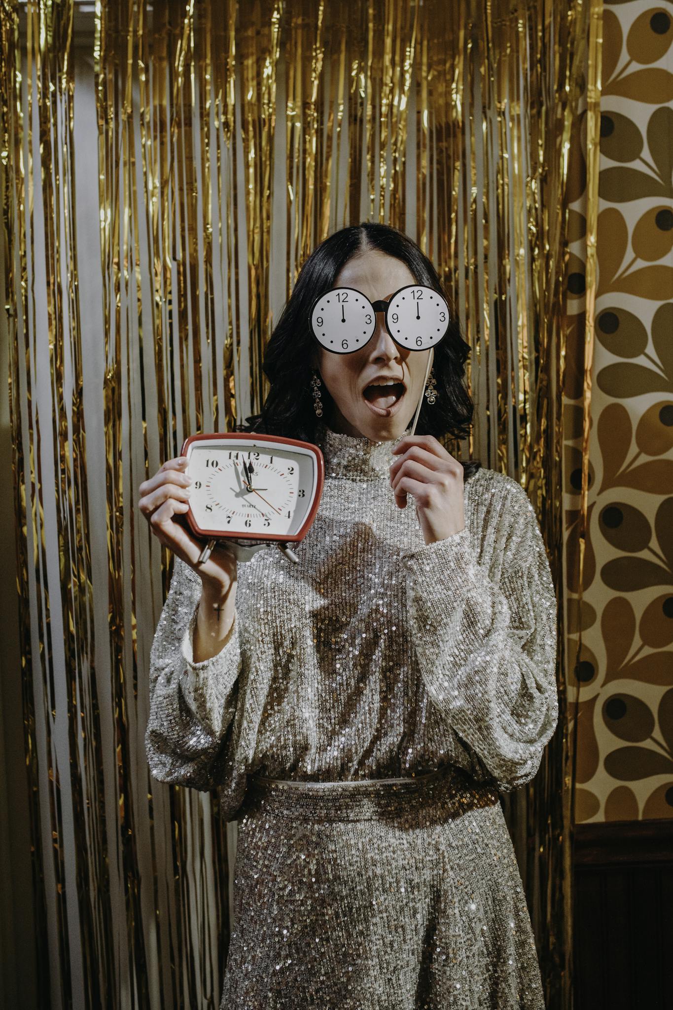 A woman in glamorous attire celebrates New Year's Eve with festive decor and clock glasses.